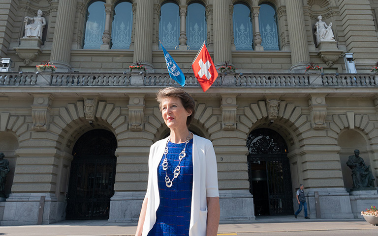 La présidente de la Confédération Simonetta Sommaruga devant le Palais fédéral, où flottent les drapeaux de la Suisse et de l’ONU.